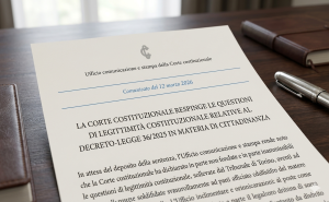 Imagem fotográfica de um documento oficial da Corte Constitucional Italiana, datado de 12 de março de 2026, posicionado sobre uma mesa de escritório de madeira escura ao lado de uma caneta tinteiro. O título do documento, 'Ufficio comunicazione e stampa della Corte costituzionale' e o comunicado sobre o resultado do julgamento do Decreto-Lei 36/2025 relativo à cidadania italiana estão visíveis, confirmando a rejeição das questões de legitimidade constitucional levantadas pelo Tribunal de Turim. A imagem tem um estilo formal e profissional, com uma profundidade de campo rasa